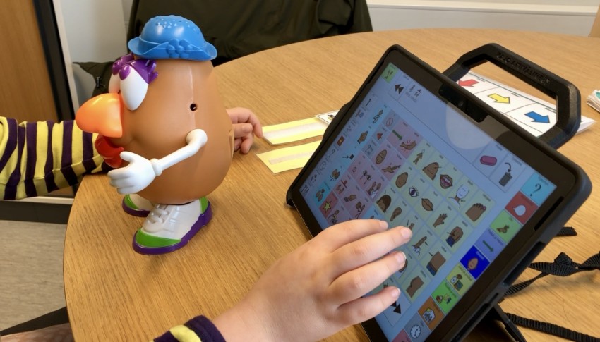 Lapsi käyttää sähköistä kommunikoinnin apuvälinettä Mr. Potato Head -leikissä.